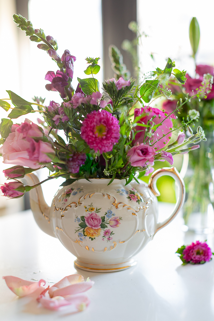 Beautiful antique floral teapot used as a vase holding a beautiful flower arrangement.